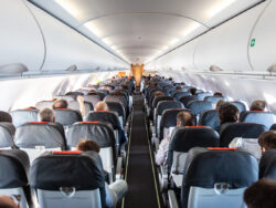 Blick durch den Gang im Flugzeug, rechts und links des Ganges sieht man Sitzreihen und sitzende Passagiere