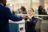 Lachende Frau des Flugzeugpersonals am Check-In Schalter gibt Person Ausweis zurück