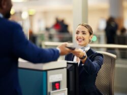 Lachende Frau des Flugzeugpersonals am Check-In Schalter gibt Person Ausweis zurück