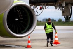 Mitarbeiter auf dem Rollfeld stellt Leitkegel neben einem Flugzeug auf