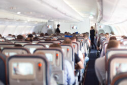 Innenraum des Flugzeugs mit Sitzreihen, sitzenden Personen und zwei Mitarbeitenden des Flugzeugs